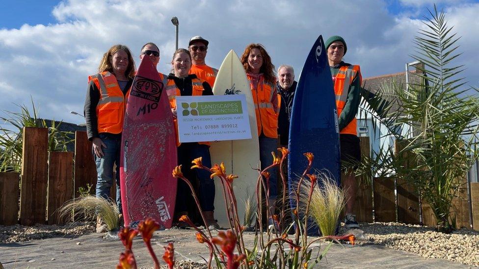 People wearing high-vis jackets with surfboards