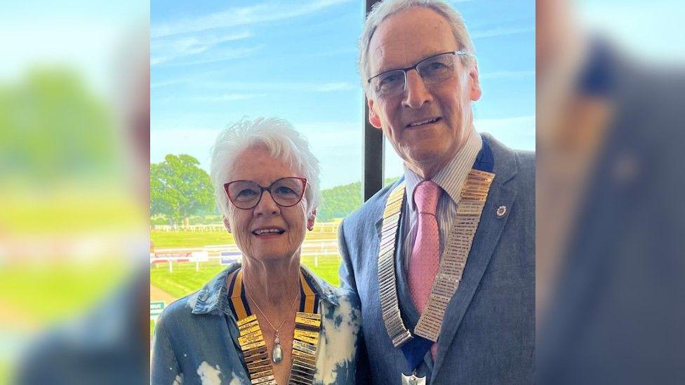 Peter and Sylvia Renshaw, both wearing ceremonial neck chains, smiling into camera