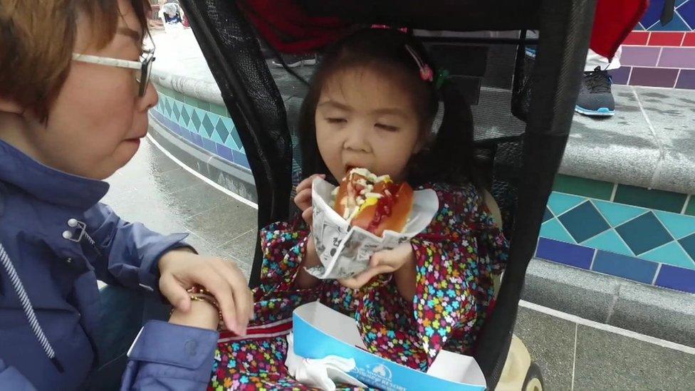 Toddler in a pram tucks into a hot dog as her mother watches, during the opening of the park.