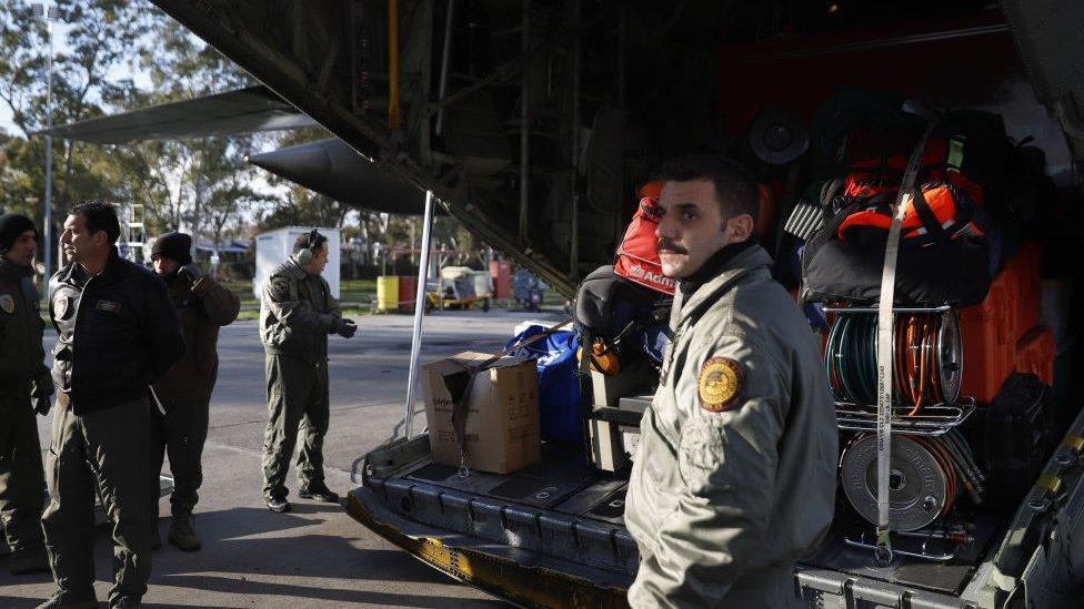 A Greek soldier stands near a plane being loaded with supplies