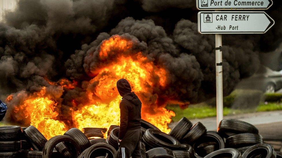 A fishermen from the French city of Boulogne walks past burning tyres blocking access to the port of Boulogne-sur-Mer on January 25, 2018,