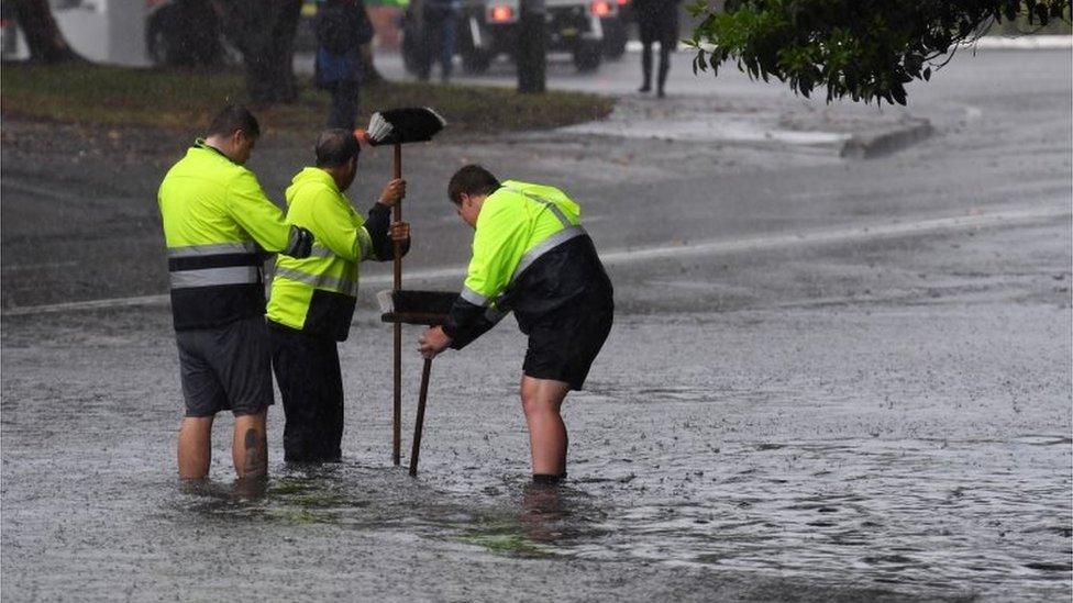 Council workers standing in ankle-deep water attempt to clear a drain