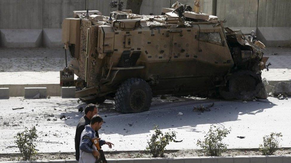 Afghan security forces walk past a damaged Nato military vehicle at the site of a suicide car bomb blast in Kabul (11 October 2015)