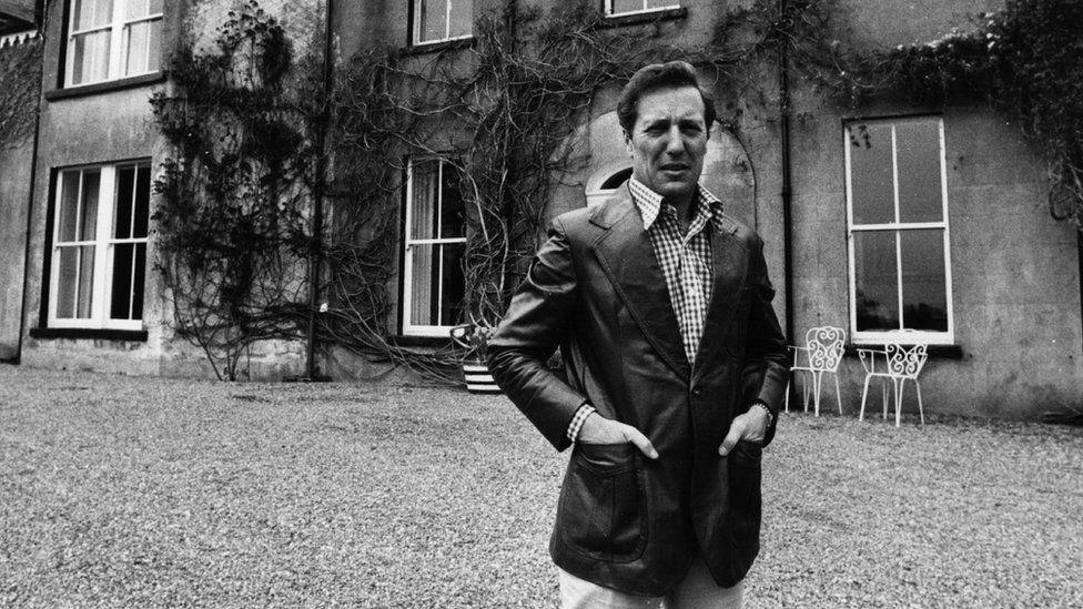 Frederick Forsyth is shown in a black and white photo outside his home.