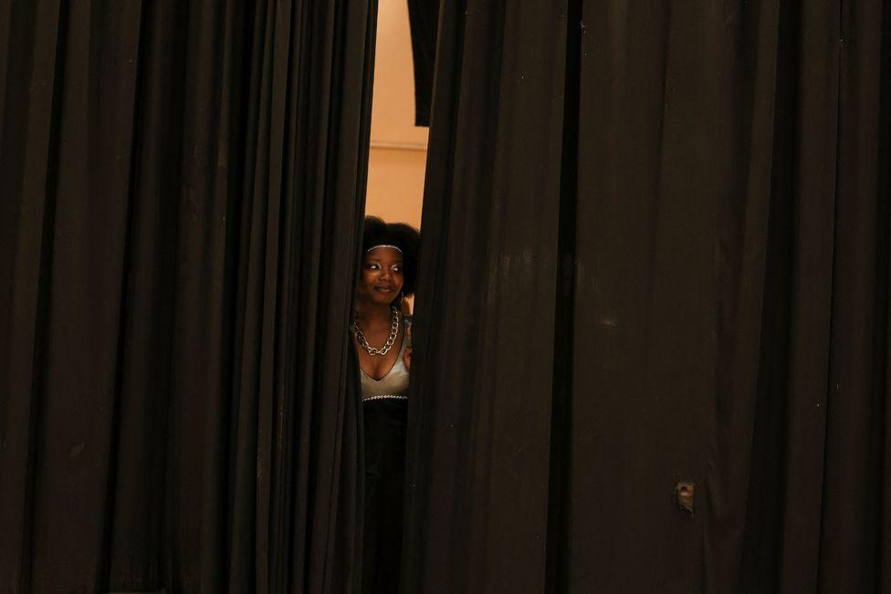 A participant looks through a curtain during their talent show on World Homeless Day at the Parow Civic Centre, in Cape Town, South Africa, October 10, 2024. 