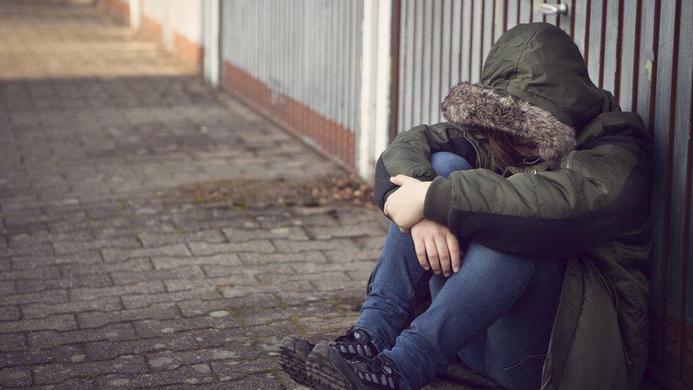 Person sitting on the street in a hooded jacket (stock image)