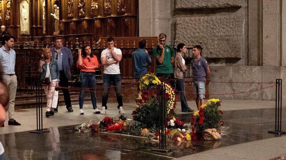 People stand at look at Franco's tomb, which is covered with flowers