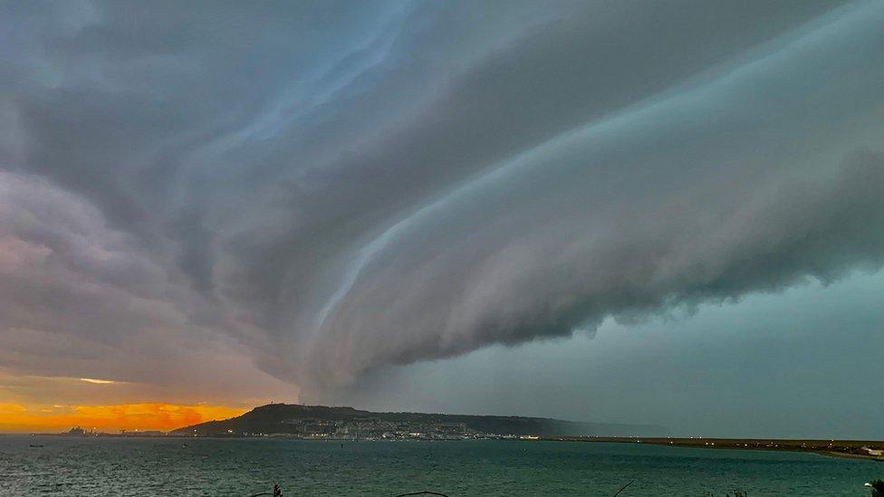 A looming shelf cloud with a red sunset in the background.