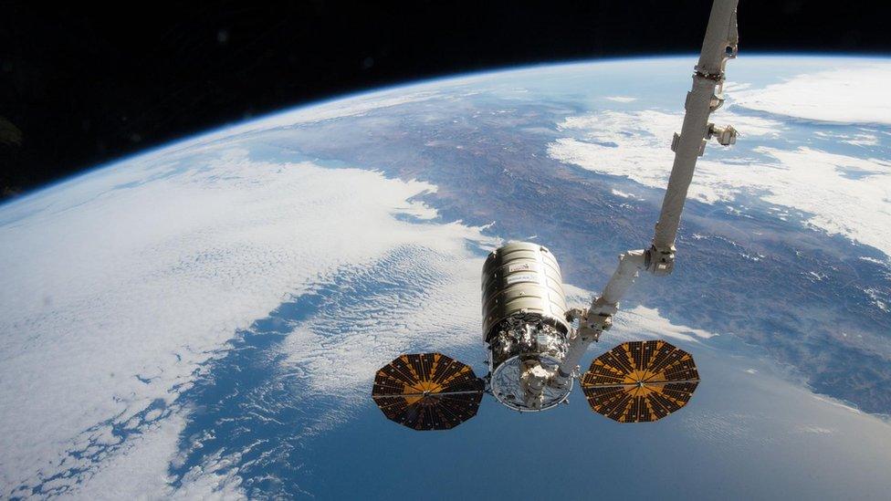 A spacecraft at the end of the Canadarm2 suspended above planet Earth.