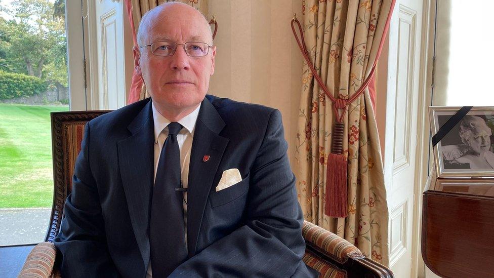 Sir John Lorimer sitting next to a photograph of the Queen