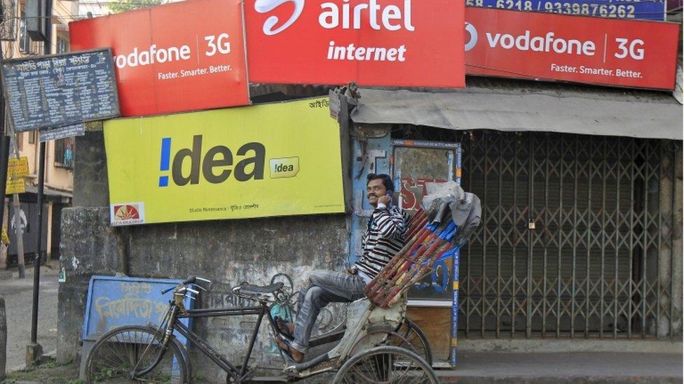 A rickshaw puller speaks on his mobile phone as he waits for customers in front of advertisement billboards belonging to telecom companies in Kolkata in this February 3, 2014 file photo