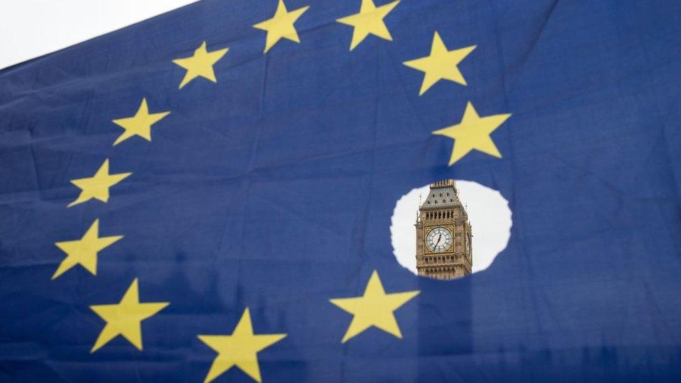 An EU flag with one of the stars symbolically cut out in front of the Houses of Parliament