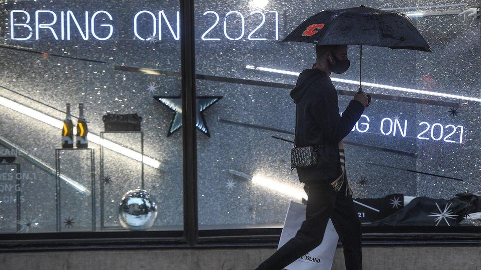 A man with an umbrella is seen walking past a shop display with a sign reading 'Bring on 2021' on December 14, 2020 in London