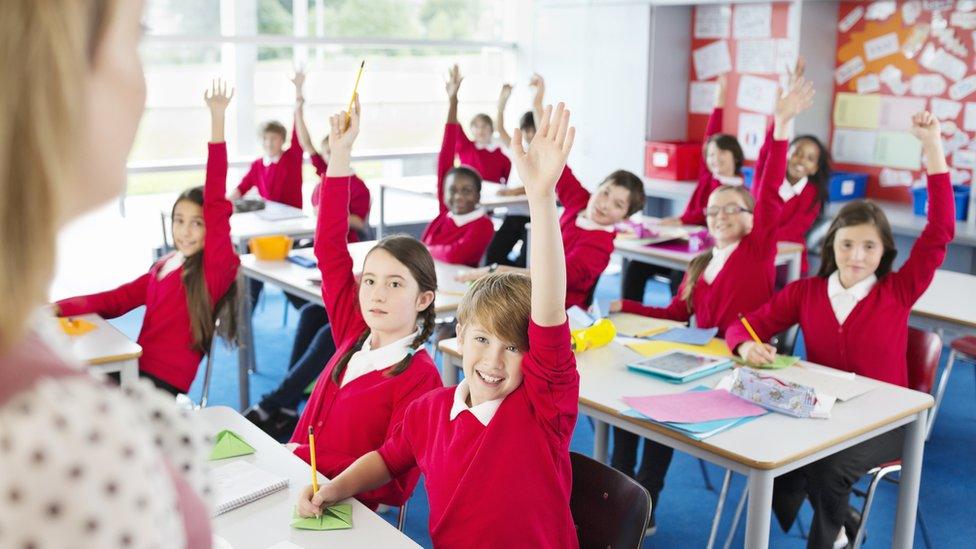 Students with hands raised in classroom - stock photo