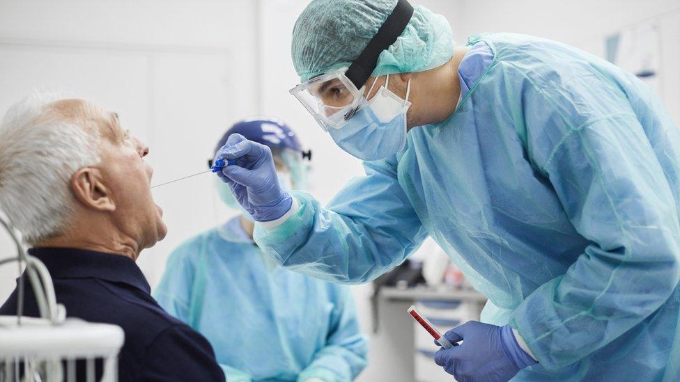 Doctor taking throat swab test from male patient. Medical worker is in protective workwear. They are at hospital during epidemic.