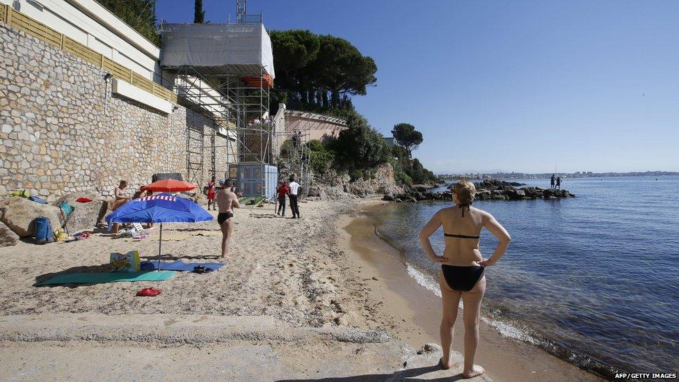 People stand as workers disassemble an elevator on the public beach near the Saudi King"s villa in the Golfe-Juan seaside resort in Vallauris, southeastern France, on August 3, 2015.