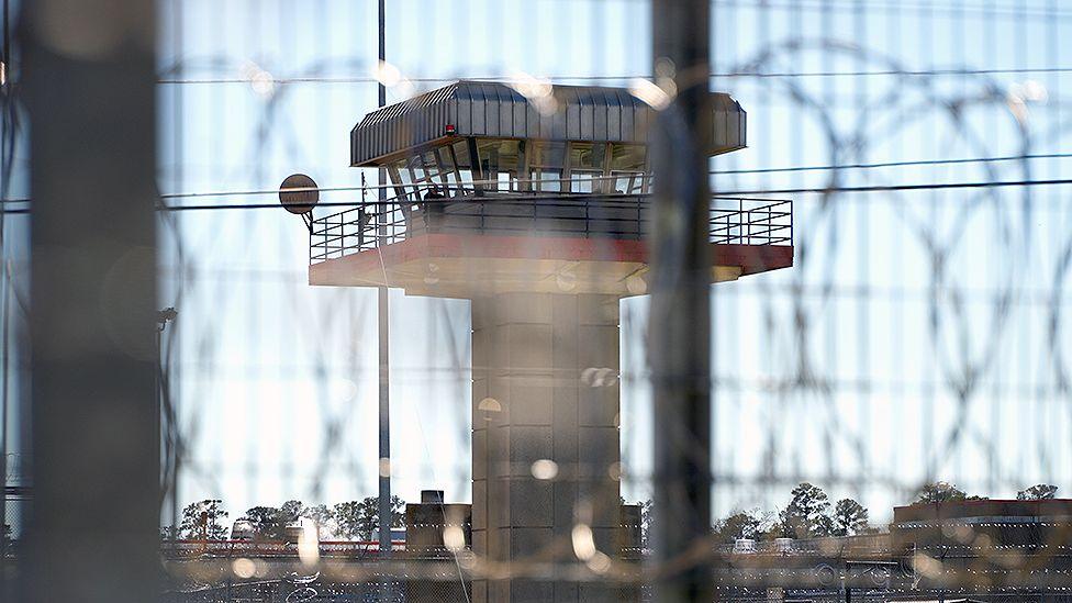 A concrete watchtower is seen through barbed wire on the perimeter fence at Estelle Supermax Penitentiary