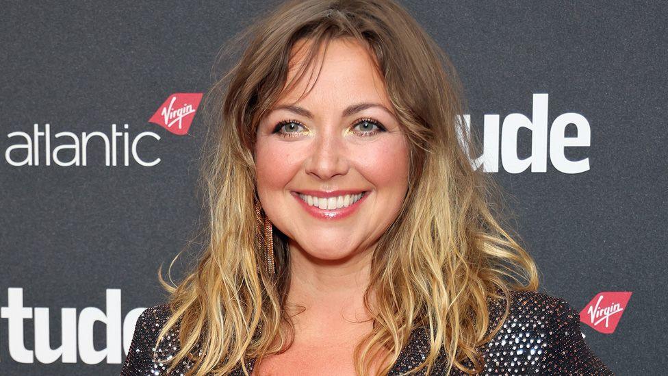 Charlotte Church smiles at the camera. She has long blonde hair and is wearing a black sparkly top.