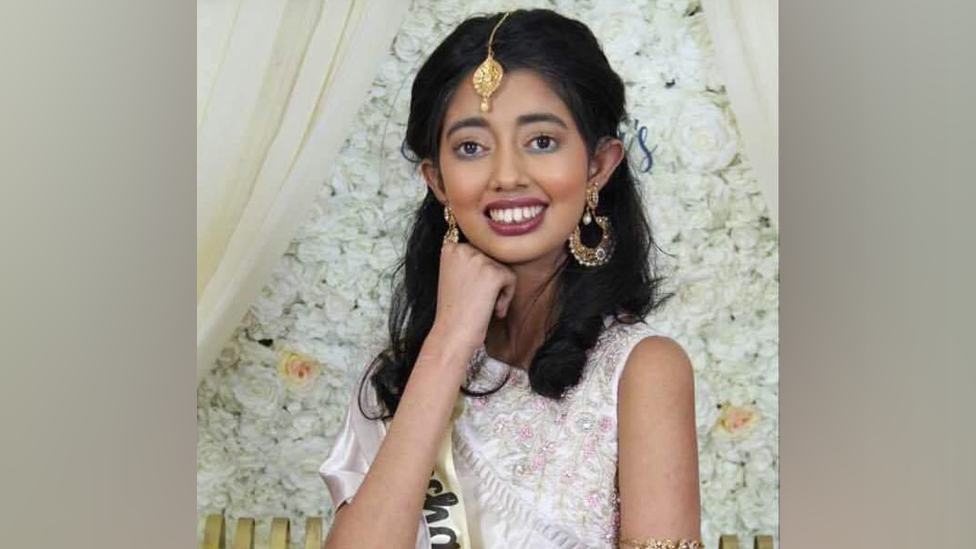 Sudiksha Thirumalesh smiling in a white dress with an embroidered floral design and wearing gold jewellery 