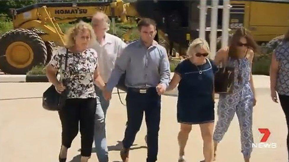 Thomas Keating arrives at a police station in Thailand with members of both families