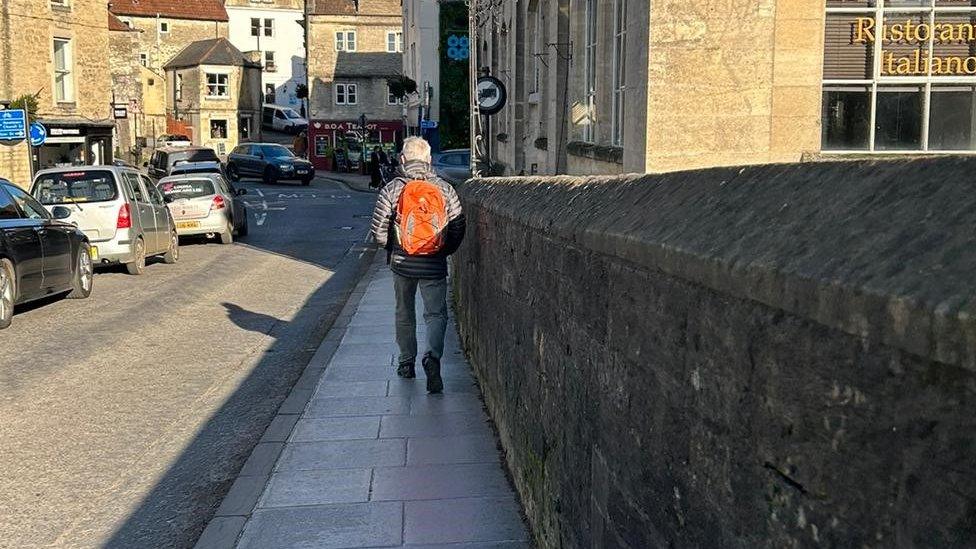 A person walking on the pavement on the bridge, with a queue of traffic on the other side