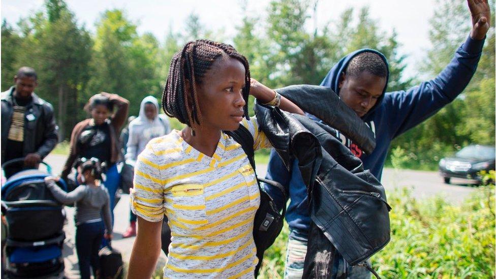 Refuges raise their hands as they illegally cross the US-Canada border