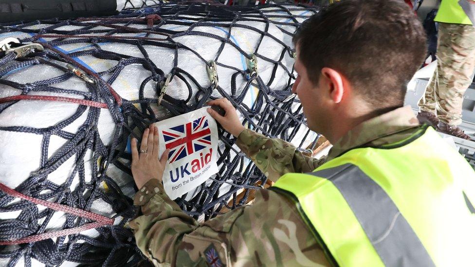 An aid-worker labels supplies with a 'UK aid' sign