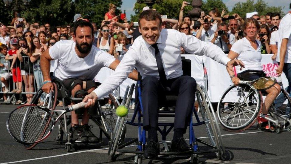 French President Emmanuel Macron returns the ball while sitting in a wheelchair as he plays tennis on the Pont Alexandre III in Paris, France, on 24 June 2017.