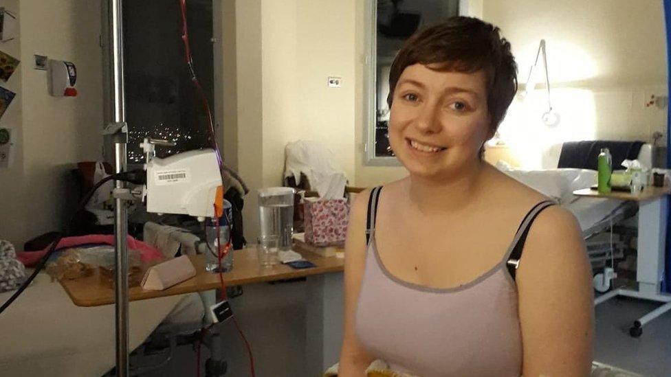 Lauren Lester in a hospital bed, sitting up an smiling at the camera