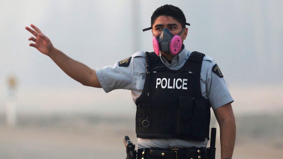 A police officer wears a mask to protect himself from smoke from the wildfires as he directs traffic near Fort McMurray (07 May 2016)