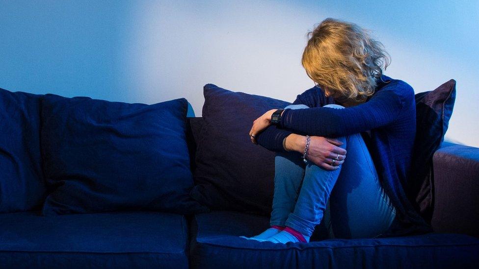 Woman sitting on a sofa clutching her knees with her head bowed