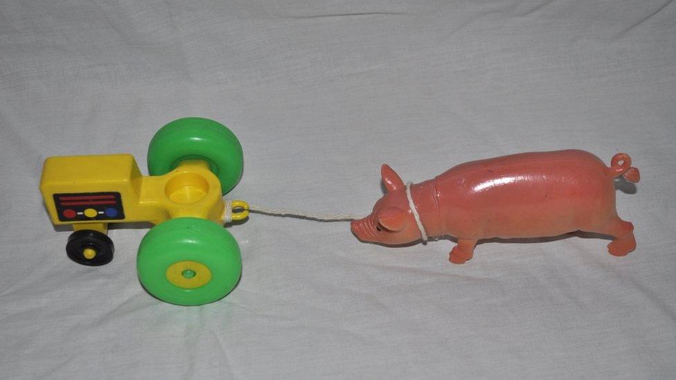 A toy tractor pulls a pig with a piece of string.