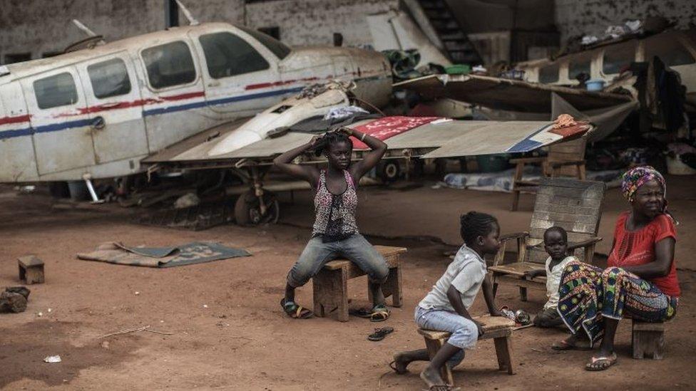 Internally Displaced People (IDP) sit near the wreckage of a light plane at the Mpoko IDP camp in Bangui on November 26, 2015, ahead of a historical visit by the pope.