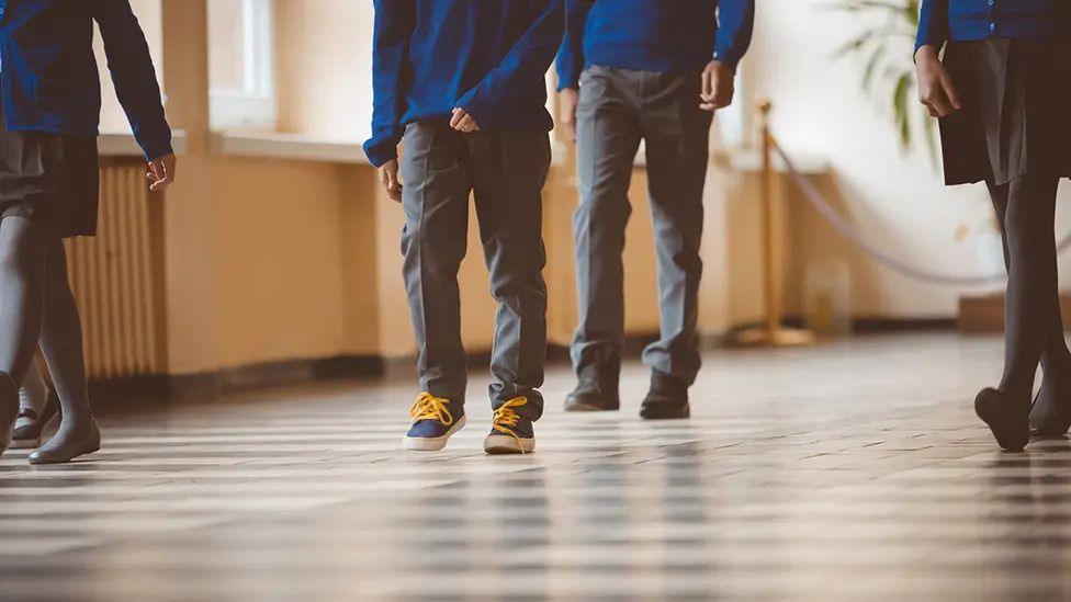 Kids walking through a hallway in school uniform.