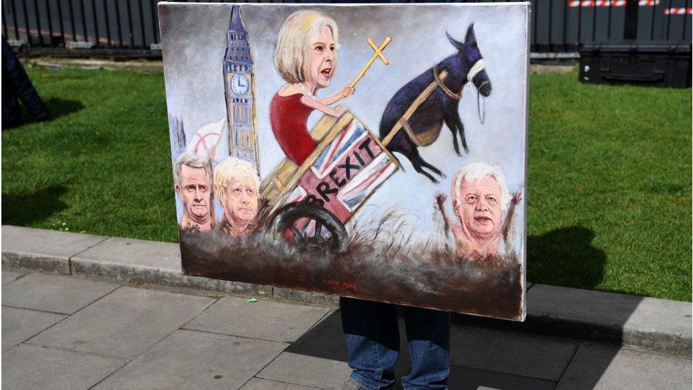 Political artist Kaya Mar holds a painting depicting the faces of British Prime Minister Theresa May, British Foreign Secretary Boris Johnson, Britain's Secretary of State for Exiting the European Union (Brexit Minister) David Davis and Britain's International Trade Secretary Liam Fox