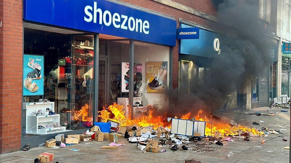 A Shoezone shop in Hull with broken windows and boxes of shoes burning on the pavement outside