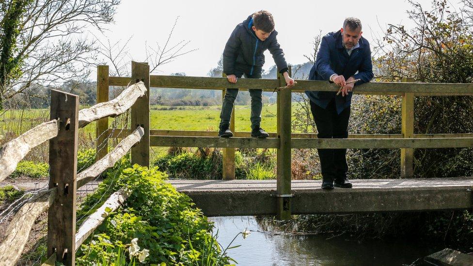 father and son play pooh sticks on a wooden footbridge