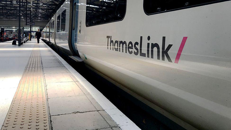 The side view of a Thameslink train at a station platform with a lone passenger walking towards it in the distance