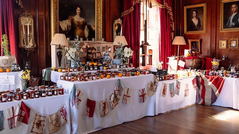 Tables with white clothes and old-fashioned Union Flag bunting with hundreds of jars of marmalade on them. 