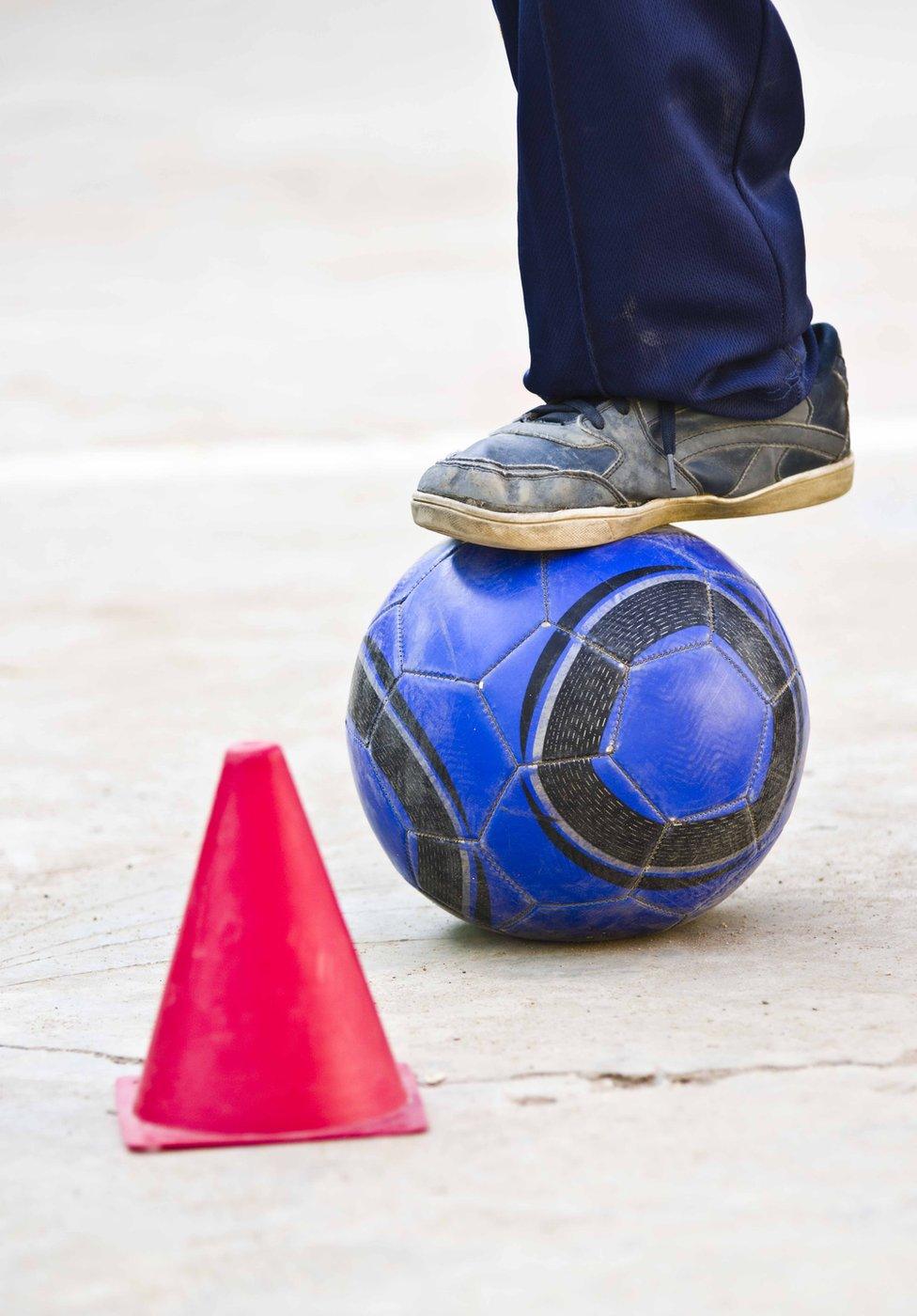 A boy's foot is seen dribbling a football around a cone