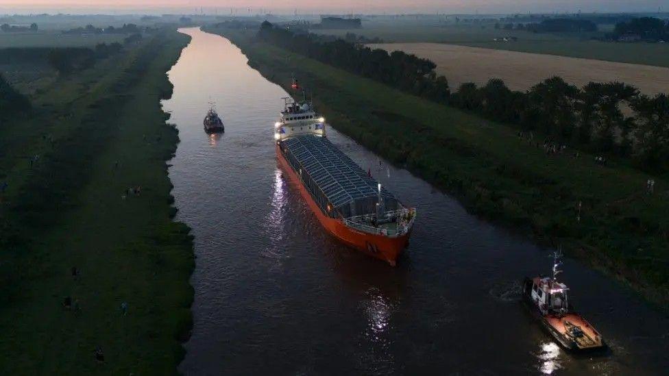 The picture has been taken at nighttime and shows the Baltic Arrow cargo ship and two smaller boats in the river.