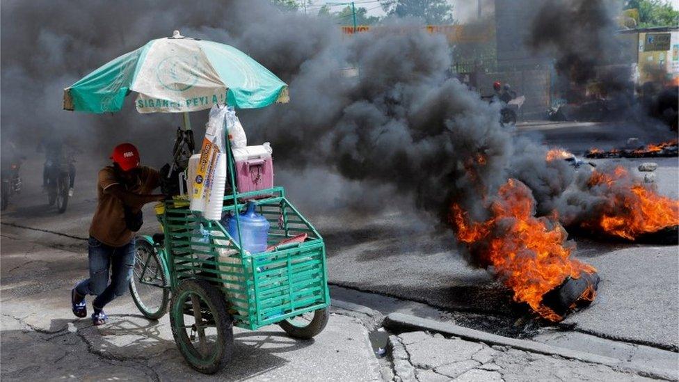 man pushes his street stand past a burning road block as anger mounted over fuel shortages that have intensified as a result of gang violence, in Port-au-Prince, Haiti, July 13, 2022