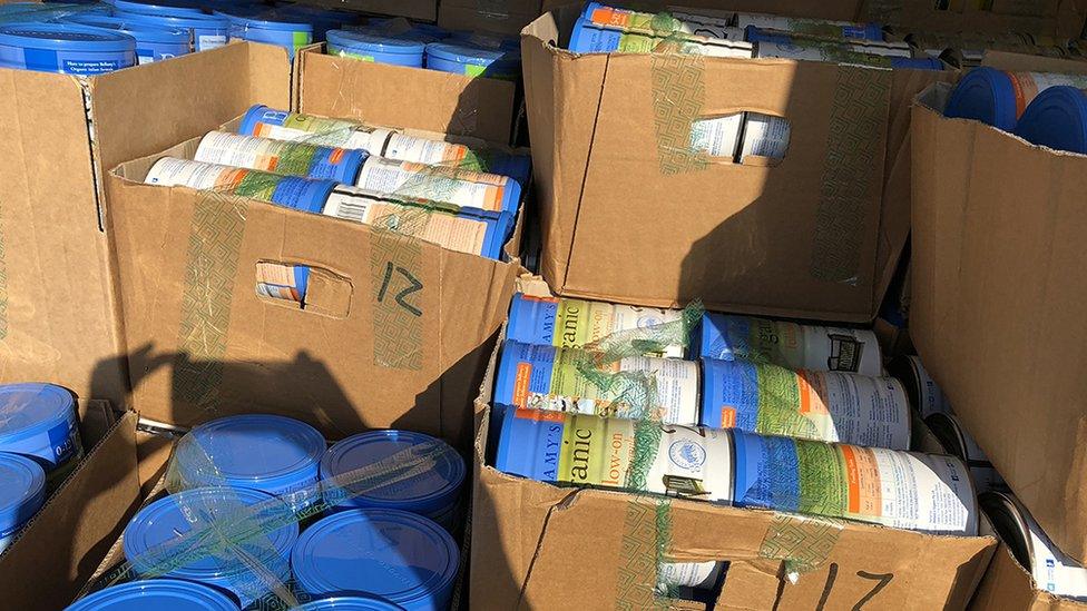 Tins of baby formula in boxes in a vehicle