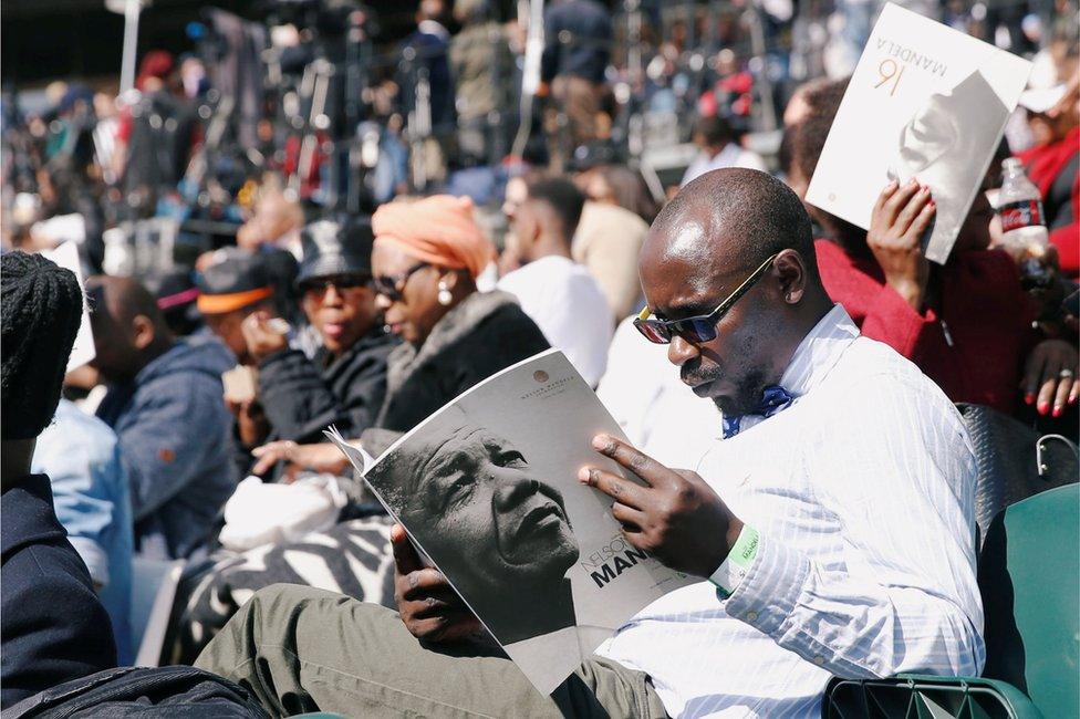 A man holds a program as crowds gather to hear former U.S. President Barack Obama delivering the 16th Nelson Mandela annual lecture, marking the centenary of the anti-apartheid leader's birth, in Johannesburg, South Africa July 17, 2018.