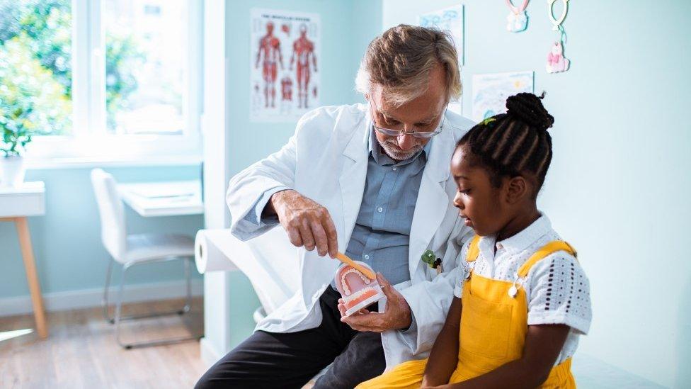 A dentist teaching a child how to brush their teeth.