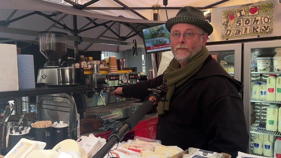 Robin Smith stood behind rows of cheeses in a green hat