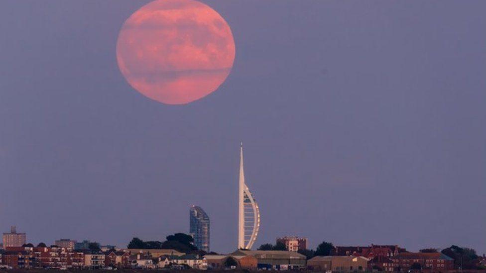 Buildings with white tower standing in centre and large moon with orange hues