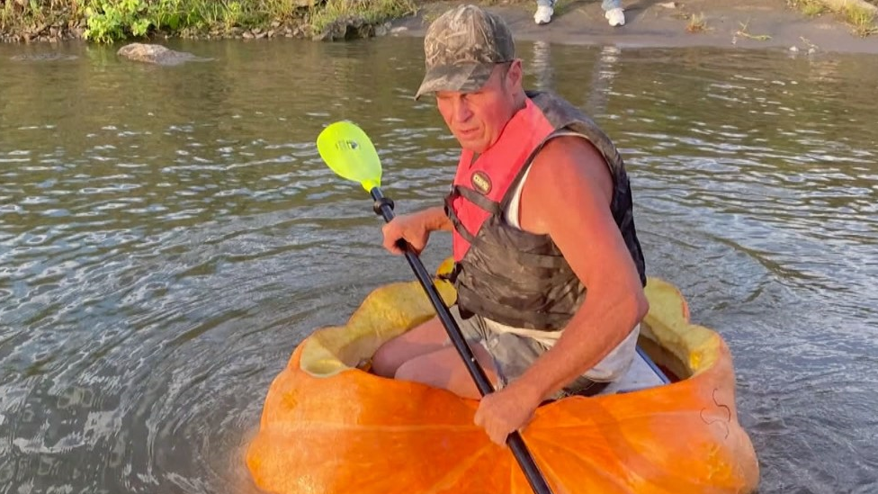 A man riding in a giant pumpkin down the river.