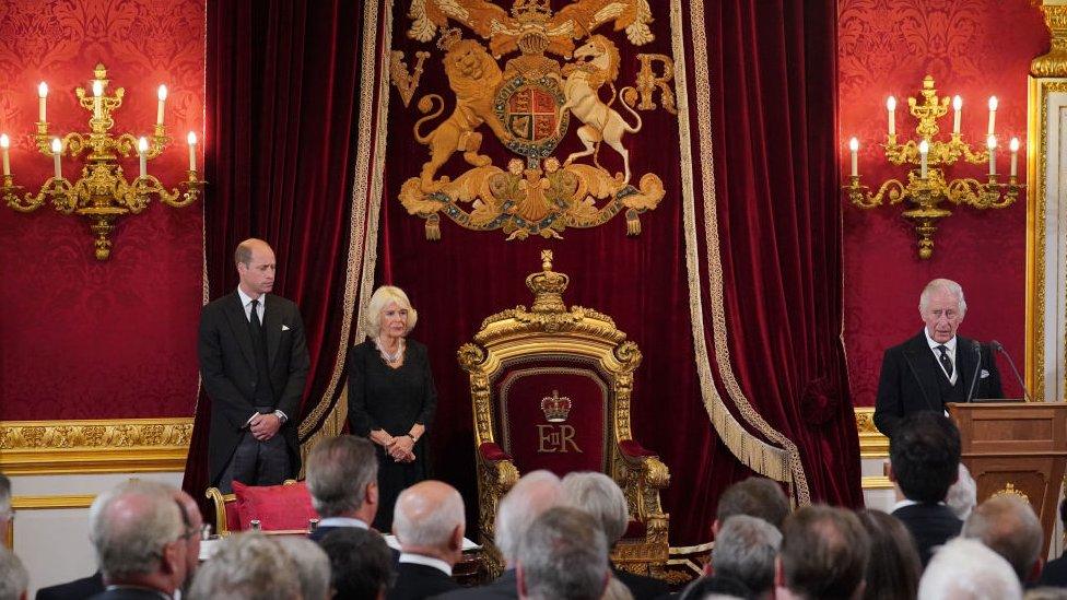 Prince Charles stood next to his throne with Camilla and Prince William up with him