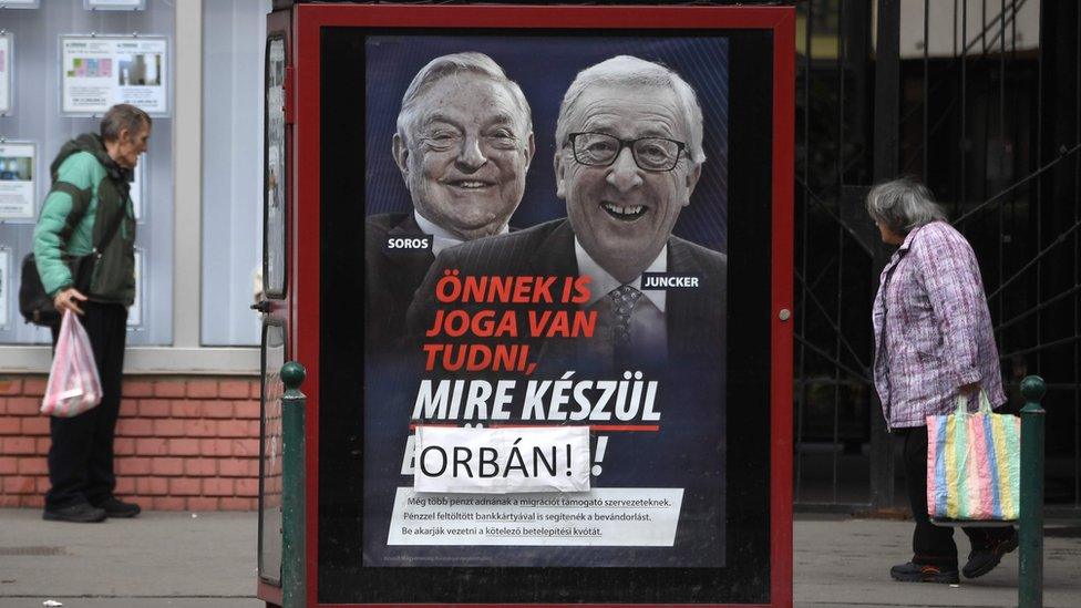 A poster featuring Jean-Claude Juncker and George Soros is seen with a piece of paper with Orban's name on it taped over the word "Brussels", changing its meaning